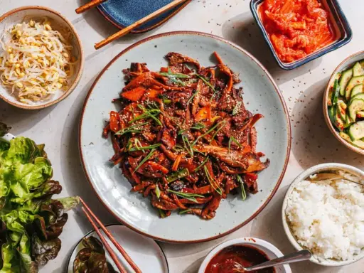 Ein köstliches koreanisches BBQ-Rezept mit gebratenem Fleisch, Beilagen wie Kimchi, Gurkensalat, Sprossen und Reis.