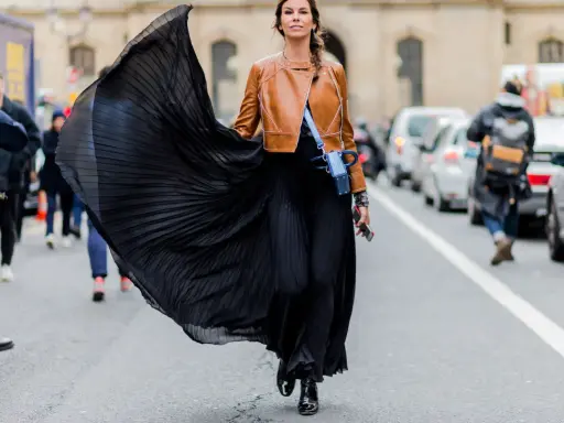 Donna con gonna nera plissettata e giacca in pelle marrone, un look audace che esprime la sua lybido abbigliamento.