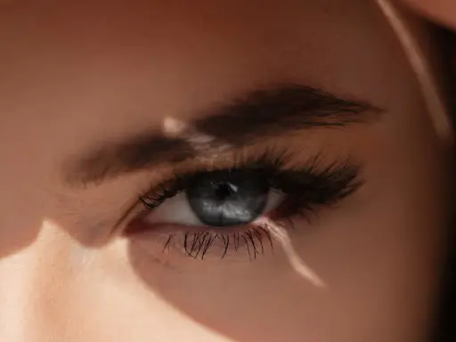 Un œil bleu intense, sublimé par un microblading parfait, capte la lumière du soleil.