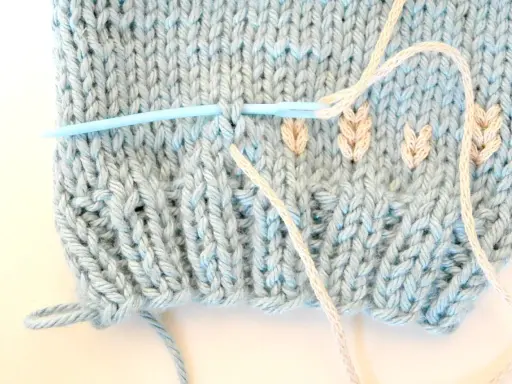 Agujas de punto plumeti dos agujas, creando un delicado diseño de hojas en tejido azul claro.