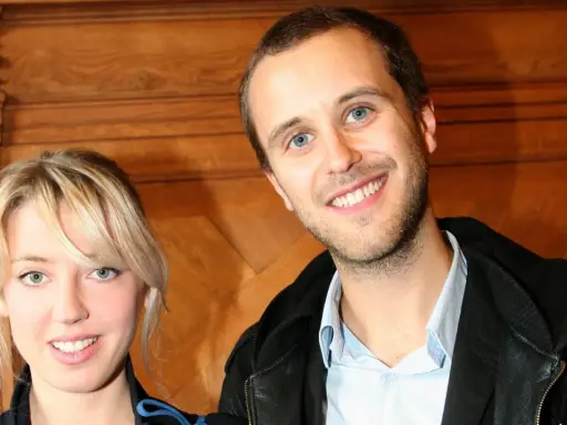 Oskar Linnros och Veronica Maggio ler mot kameran, med en träbakgrund som ger en varm känsla.