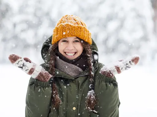 Una chica sonríe felizmente en medio de una nevada, con su gorro naranja y guantes a juego. ¡Bonitas fotos en la nieve!