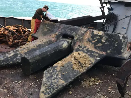 Un marin prépare une énorme ancre de bateau, expliquant comment fonctionne une ancre de bateau : elle s'enfonce dans le fond marin pour stabiliser le navire.