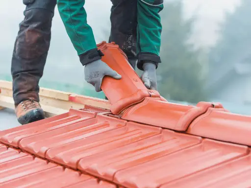 Dachówka ceramiczna w rękach dekarza. Czy remont dachu wymaga pozwolenia na budowę? Zależy od zakresu prac.