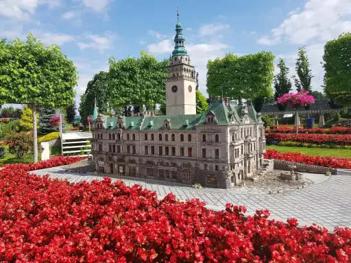 Miniatura ratusza z wieżą zegarową, otoczona czerwonymi kwiatami. Jedna z wielu atrakcji Kotliny Kłodzkiej.