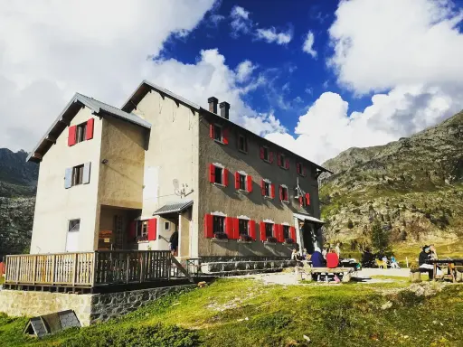 Rifugi raggiungibili in auto a Bergamo: un edificio con persiane rosse in montagna, con persone sedute fuori.