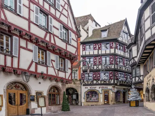 Fachwerkhäuser mit roten und weißen Fassaden in der Colmar Altstadt, geschmückt mit Lichterketten und Weihnachtsdekoration.