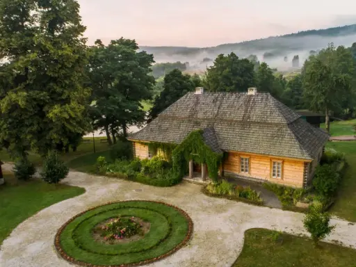 Drewniany dom, otoczony zielenią i mglistym krajobrazem, przypomina bajkowy dom ze szkła.