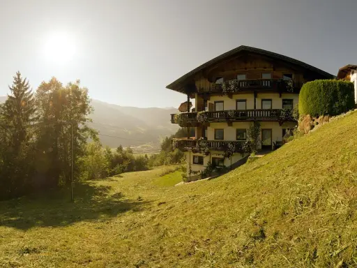 Haus im Alpenvorland mit traditioneller Architektur und Balkonen, umgeben von grünen Wiesen und Bergen.