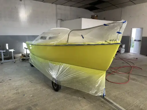 Un bateau jaune est bâché pour le repeindre. Il est sur une remorque dans un atelier.