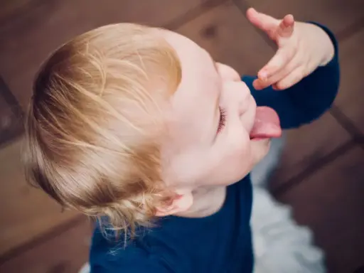 Małe dziecko nie słucha w przedszkolu, wyciąga język i bawi się jedzeniem.