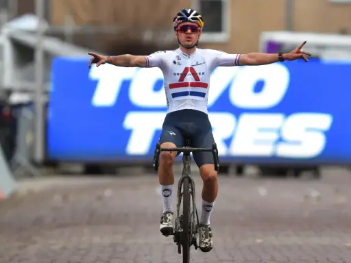 Thomas Pidcock feiert seinen Sieg mit ausgebreiteten Armen. Der Radfahrer trägt ein weißes Trikot mit britischer Flagge und dunkle Hosen.