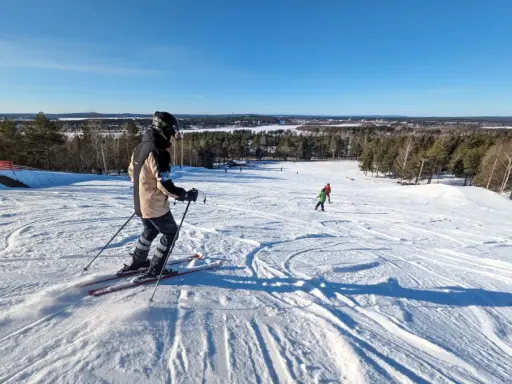 Person åker skidor i Luleå en solig dag. Barn åker skidor i bakgrunden.