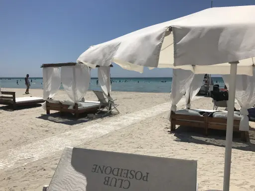 Beach cabanas with white curtains and beds on a sandy beach with the ocean in the background.