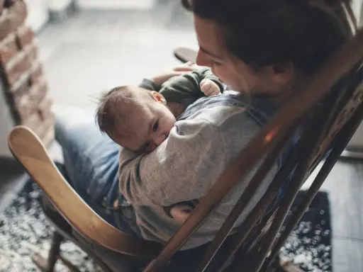 Ein Baby schläft friedlich auf dem Arm einer Person, die in einem Schaukelstuhl sitzt. Es ist, als ob die Babys im Bauch noch träumen, bevor sie die Welt entdecken.