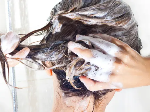 Hände massieren schaumiges, **essential shampoo** in nasses Haar.