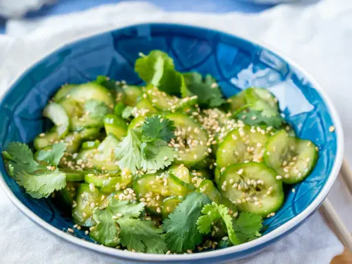 Frischer Gurkensalat mit Sojasauce, Koriander und Sesam in einer blauen Schüssel.