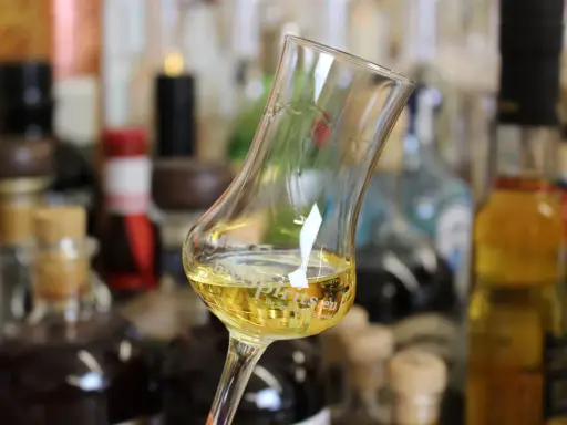 Ein Glas mit goldgelbem Wein steht vor einer Sammlung von Flaschen. Das Glas erinnert an ein Kirchenfenster, das Licht bricht.