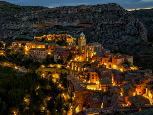 Pueblo iluminado al anochecer, ideal para planes para el puente de diciembre. Casas de piedra y tejados se asoman entre la montaña.