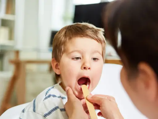 Bambino con bocca aperta durante visita medica per sospetta laringite.