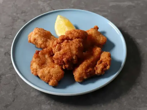 Chrupiący kurczak karaage na niebieskim talerzu, z kawałkiem cytryny.