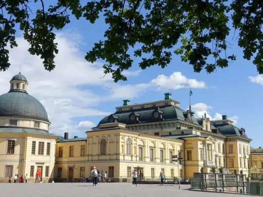 Drottningholms slott, där kungen bor, med sin imponerande kupol och gula fasader under en blå himmel med moln.