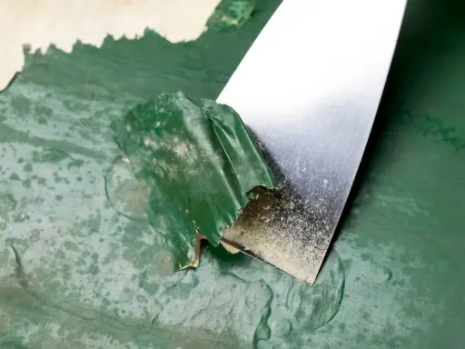 Espátula metálica retirando pintura verde descascarada de una pared. Proceso de cómo quitar pintura de la pared.