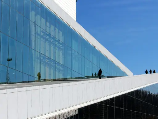 Nowoczesna architektura Uniwersytetu w Oslo z lustrzaną fasadą odbijającą niebo i ludzi.