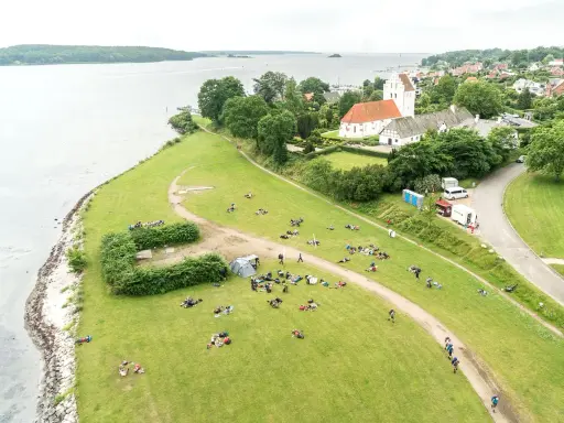 En grupp människor njuter av en paus under sin vandring i Danmark. En kyrka med tegeltak syns i bakgrunden.