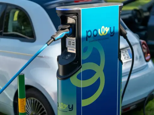 Estación de recarga para coche eléctrico con cable azul conectado. La estación tiene el logo "powy" y el lema "CHARGE THE CHANGE".