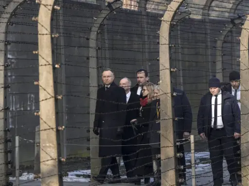 Eine Gruppe von Menschen, darunter ein Mann in einem langen schwarzen Mantel, geht hinter Stacheldraht entlang. Die Szene erinnert an die Verfolgung von Dietrich Bonhoeffer.
