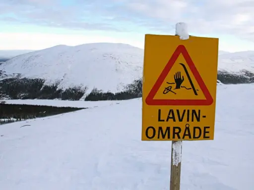 Varning för lavin vid Kebnekaise. Ett gult varningsskylt med en hand, skidor och rep i en röd triangel.