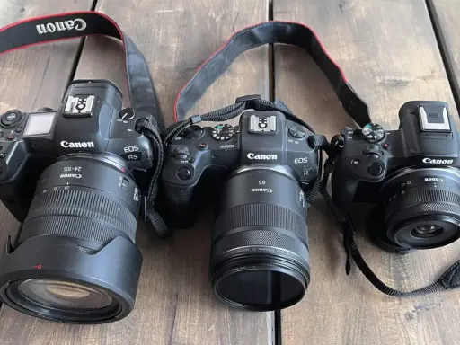 Trzy aparaty Canon EOS R, RP i R5 z obiektywami leżą obok siebie. Pełna klatka w całej okazałości.