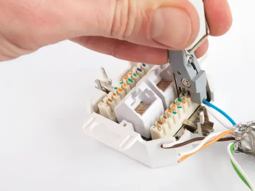 Hand legt Kabel an Netzwerkdose auf. Werkzeug drückt blaue Ader in LSA-Leiste.
