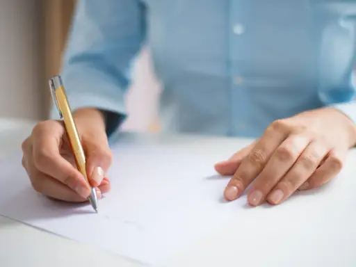 Dłoń pisze złotym długopisem na białej kartce, przygotowując się do egzaminu CAE practice tests.