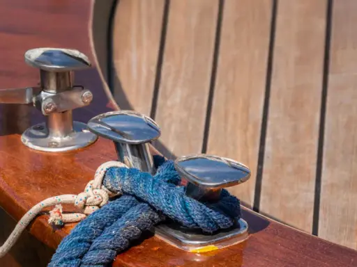 Corde bleue et blanche nouée sur des taquets chromés, prêts pour nettoyer le pont du bateau. Le bois verni brille au soleil.