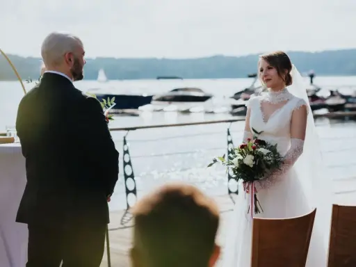 Panna młoda w białej sukni i pan młody w garniturze podczas ceremonii ślub rzymski nad jeziorem.