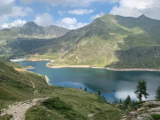 Sentiero facile tra i laghi gemelli alpini, con montagne verdi e un cielo azzurro con nuvole bianche.
