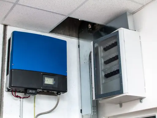 Niebieski falownik, kluczowy element instalacji fotowoltaicznej, zamontowany obok białej skrzynki z zabezpieczeniami.