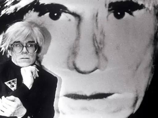 Andy Warhol, Ikone der Pop Art, posiert vor einem riesigen Porträt von sich selbst. Seine Kunstrichtung prägte die moderne Kunst.