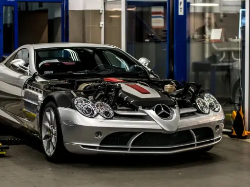 Srebrny Mercedes McLaren z otwartą maską, odsłaniającą potężny silnik, stoi w warsztacie.