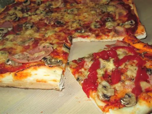 Pyszna pizza na cienkim cieście z pieczarkami i szynką, polana ketchupem. Idealna na szybki obiad.