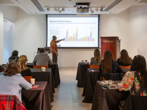 A presenter discusses market performance at Christie's, showing auction data to an audience.
