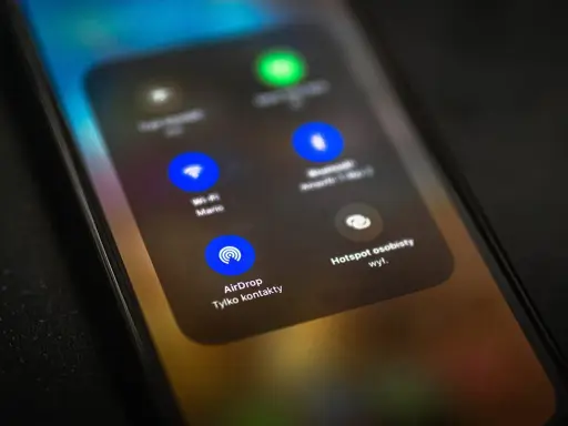 Ekran telefonu z widocznym menu, gdzie opcja AirDrop jest podświetlona. To funkcja do bezprzewodowego udostępniania plików między urządzeniami Apple.