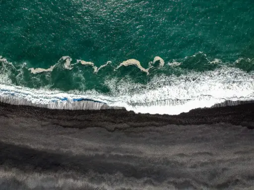 Gran Canaria: Türkisfarbenes Meer trifft auf einen dramatischen schwarzen Strand. Wellen brechen sich auf dem dunklen Sand.