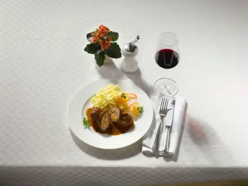 Ein Teller Rouladen mit Bandnudeln und einem Glas feinherb Wein. Dazu ein kleines Blümchen und Besteck.