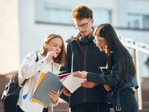 Trzech studentów dyskutuje nad notatkami, ich status ucznia widoczny w skupieniu i materiałach.