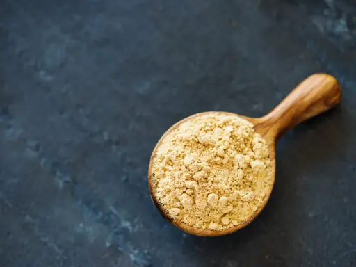 Cuillère en bois remplie de poudre de maca, évoquant ses nombreux bienfaits pour la santé et l'énergie.