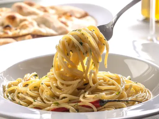 Pyszne dania z makaronem: spaghetti z ziołami i czosnkiem, na talerzu, z widocznym w tle pieczywem.