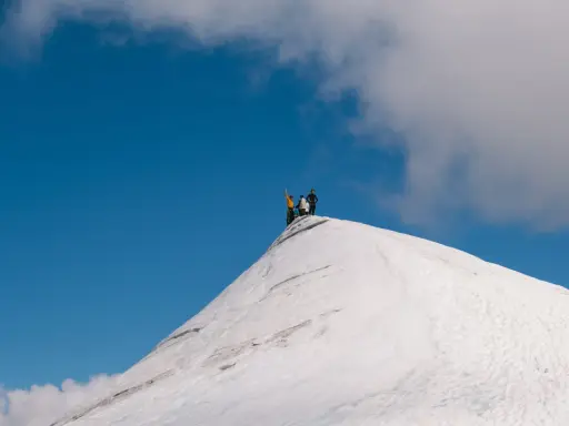 Vandrare på toppen av en snötäckt bergstopp, en vy som ger en känsla av var ligger Kebnekaise.